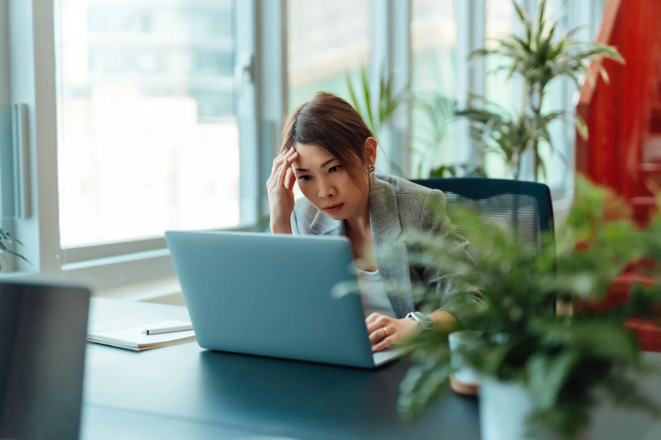 Tired Asian businesswoman working on a laptop.